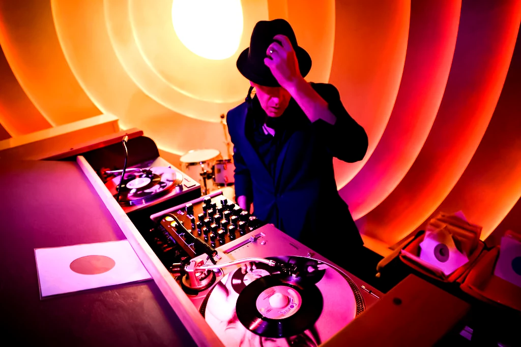DJ Turmix in a black hat, playing vinyl under orange light