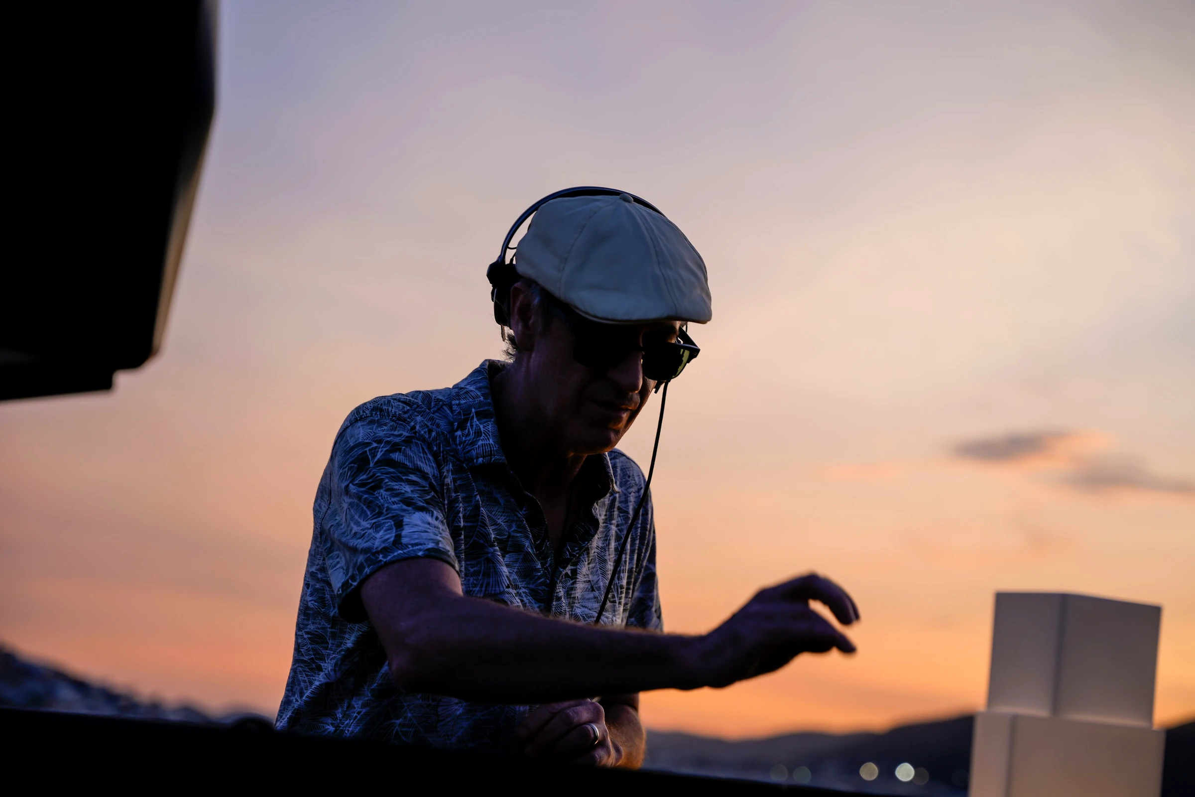 DJ Turmix at sunset, in a flat cap and headphones, playing a set